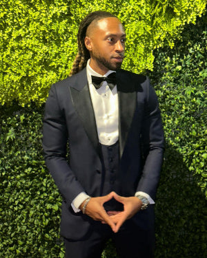 Man in a tuxedo standing against a green hedge